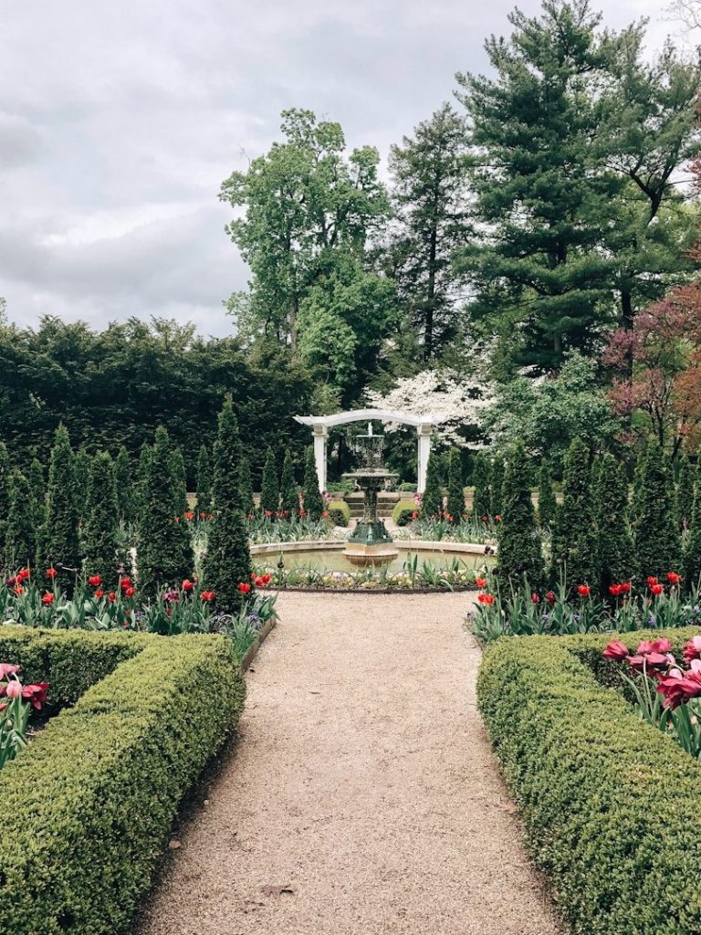 Ein gepflegter Gartenweg mit Blumenbeeten und einem zentralen Brunnen.