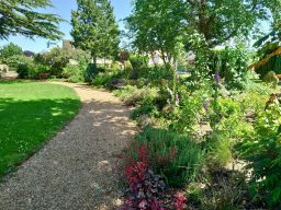 Bunten Gartenweg umgeben von Blumen und Bäumen, sonniger Tag.