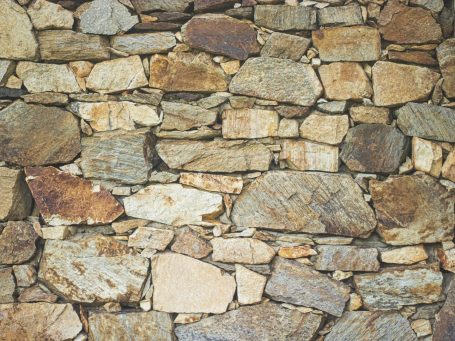 Eine Mauer aus unregelmäßig geformten, verschiedenen Steinen in erdigen Farben.