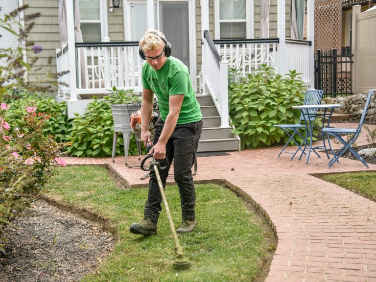 Junger Mann schneidet Gras mit einem Trimmer in einem gepflegte Garten.