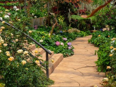Ein gepflasterter Weg führt durch einen blühenden Garten mit verschiedenen Blumen.