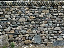 Eine Steinmauer aus unterschiedlichen, grob bearbeiteten Steinen in verschiedenen Farben.