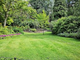 Grüner Garten mit Bäumen, Blumenbeeten und gepflegtem Rasen.